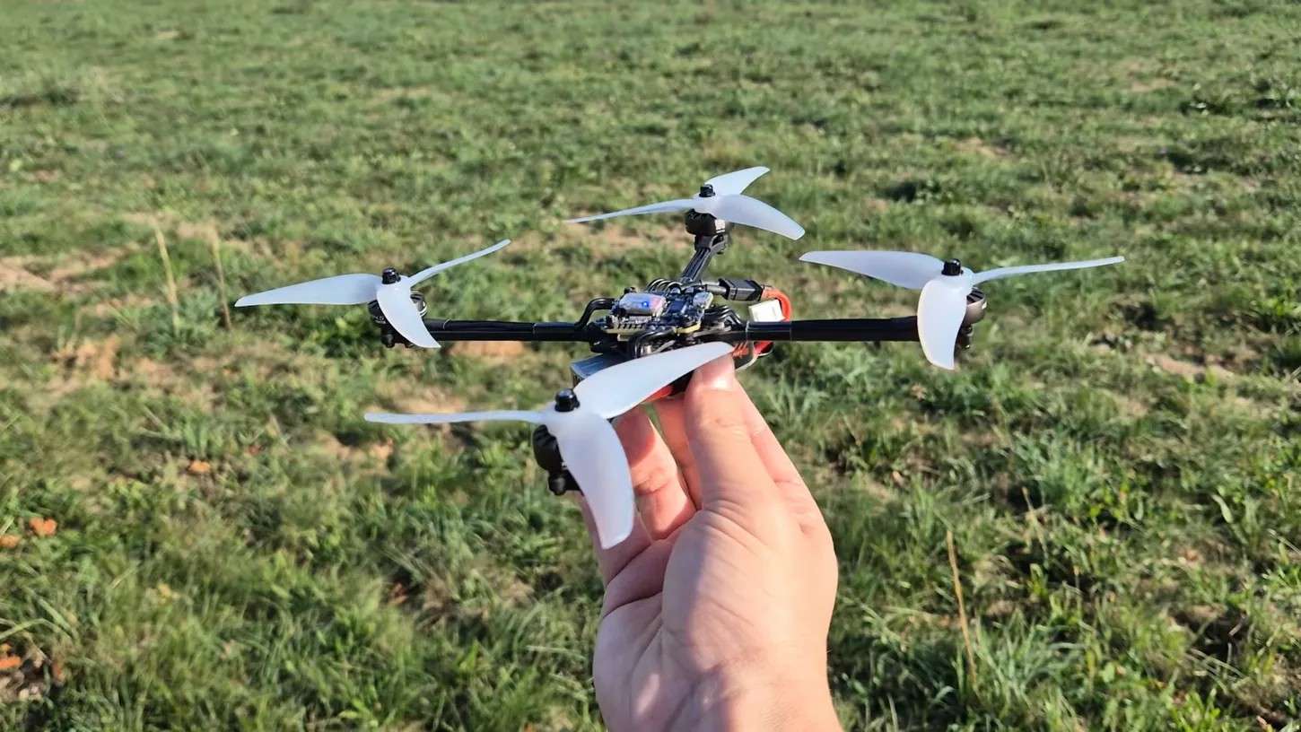 Mano sujetando el dron FPV de 5 pulgadas y 160 gramos de quadmovr, con hélices tribala blancas, sobre un campo de hierba